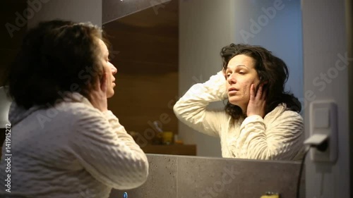 Woman standing in front of the mirror in the bathroom and looks tired
