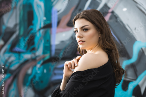 Beautiful woman against street art graffiti wall with naked shoulder