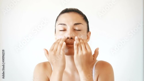 Beautiful brunette woman applying cream on her face