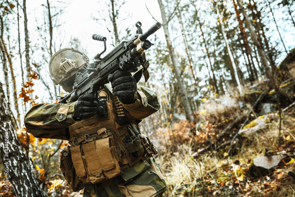 Norwegian Rapid reaction special forces FSK soldier firing in the forest. Field camo uniforms, combat helmet and eye-wear goggles are on