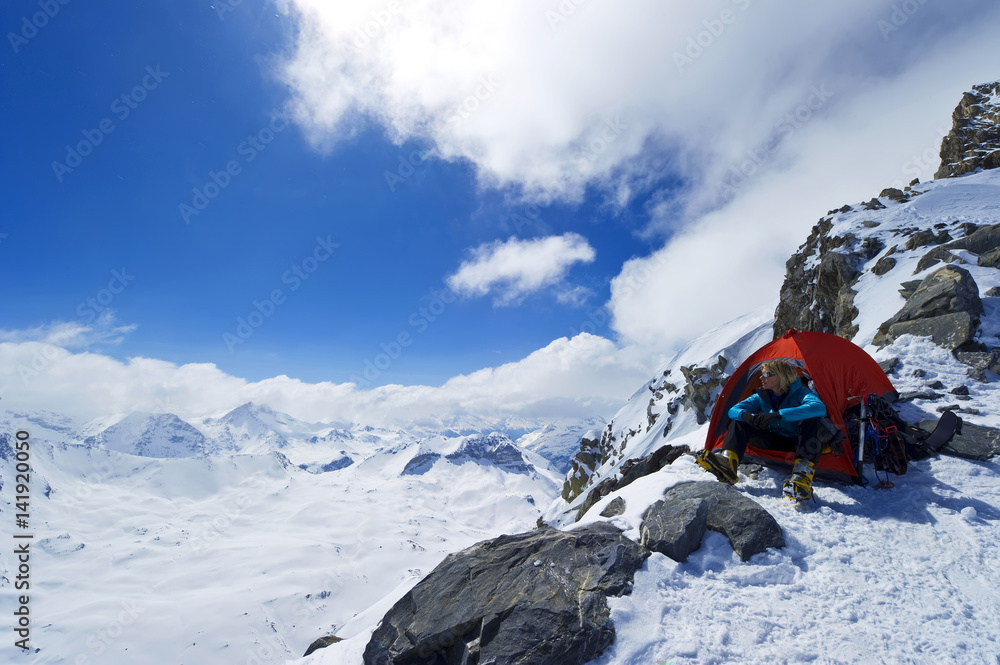 A women camping at high altitude sits in her tent and enjoys the mountain views.
