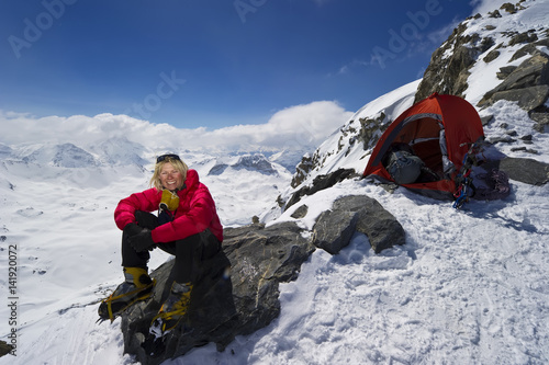 A female mountaineer camping at high altitude smiles and enjoys herself.
