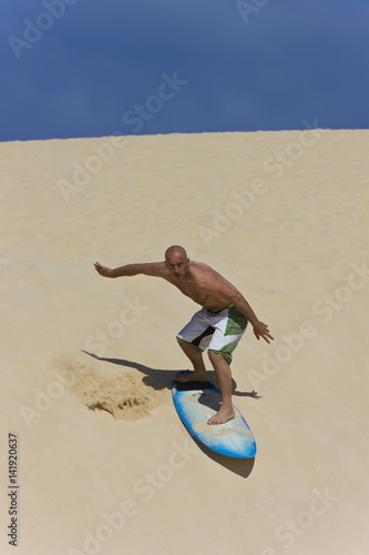 Photography A surfer sand boarding his way down a dune on the way to the Ocean