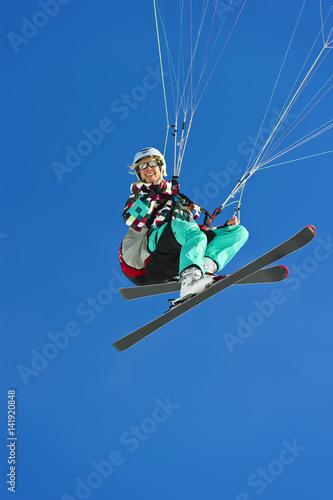 A female Paraglider pilot smiles in flight with her skis on for take off/landing.