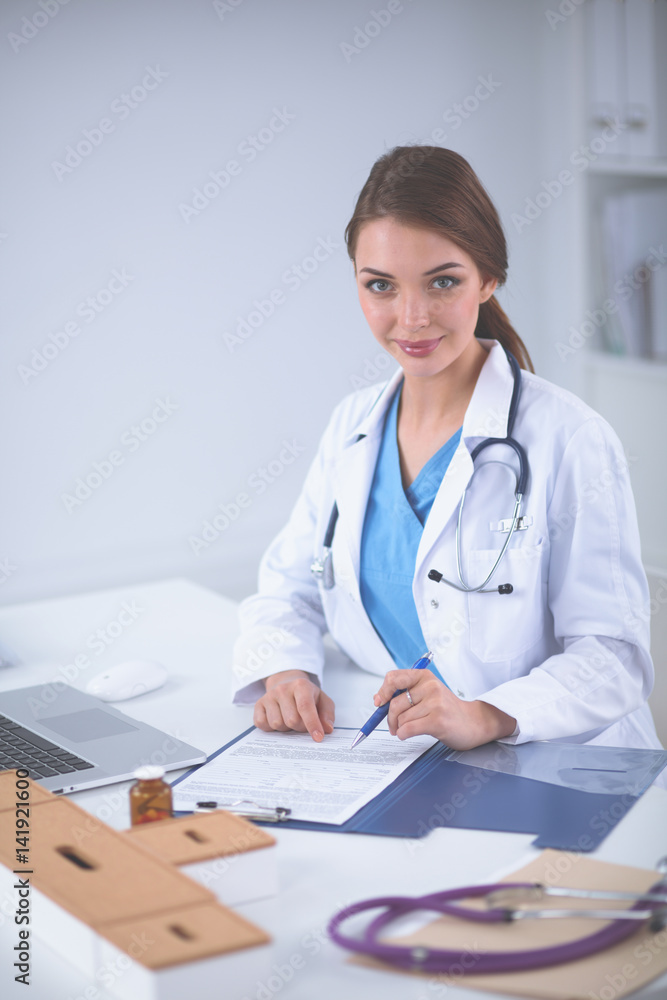 Beautiful young smiling female doctor sitting at the desk and writing Beautiful young smiling female doctor sitting at the desk and writing