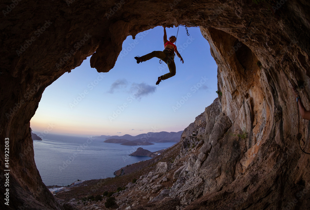 Young woman climbing in cave at sunset