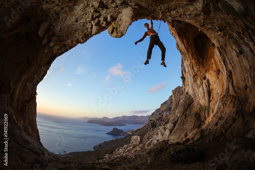 Rock climber gripping handhold on ceiling in cave
