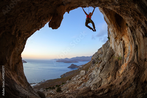 Young woman climbing on ceiling in cave at sunset
