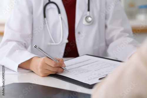 Close up of a female doctor filling up an application form while consulting patient. Medicine and health care concept