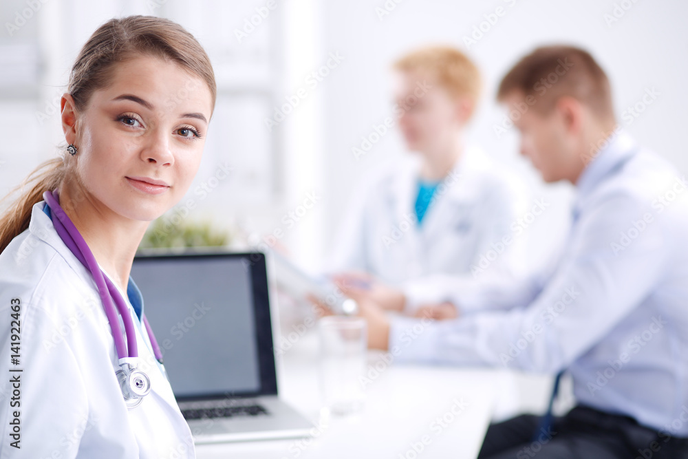 Beautiful young smiling female doctor sitting at the desk Beautiful young smiling female doctor sitting at the desk