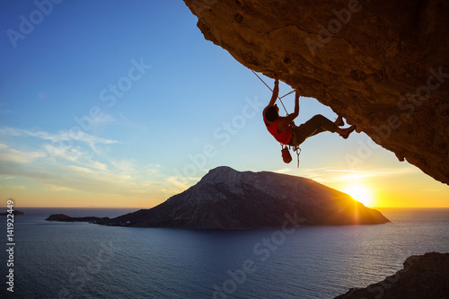 Foto Young man climbing overhanging cliff at sunset