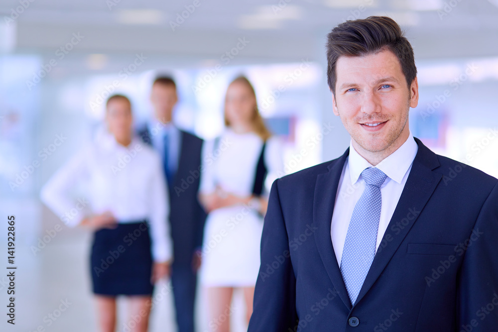 Portrait of young businessman in office with colleagues in the background Portrait of young businessman in office with colleagues in the background
