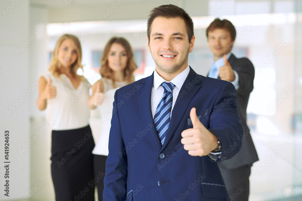 Successful young business people showing thumbs up sign while standing in office interier Successful young business people showing thumbs up sign while standing in office interier