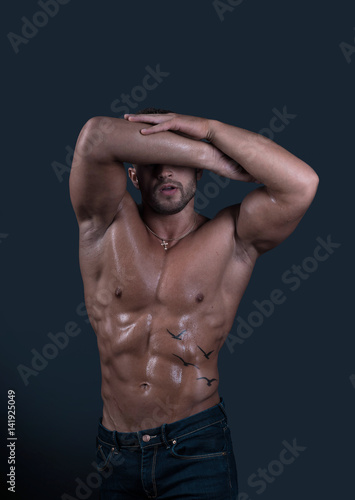 Young attractive sexy male fitness model demonstrates his handsome athletic wet muscular body	