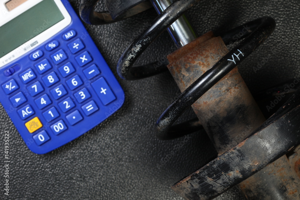 The old and dirty shock absorber cover with rust put beside calculator  represent the car part and maintenance budget concept related idea. foto de  Stock | Adobe Stock