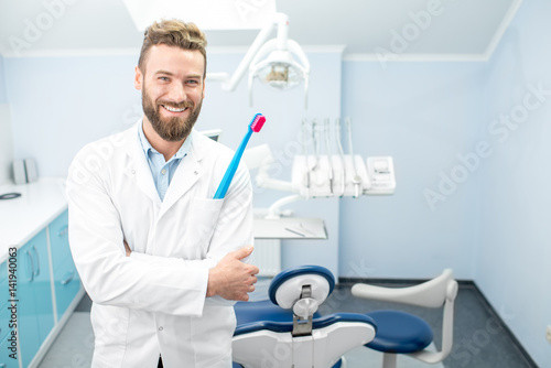 Portrait of handsome dentist in uniform with big toothbrush at the dental office