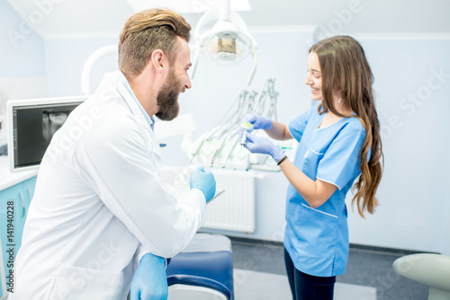 Handsome dentist with young female assistant in uniform prepairing for the job at the dental office