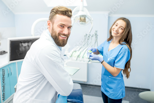 Handsome dentist with young female assistant in uniform prepairing for the job at the dental office photo