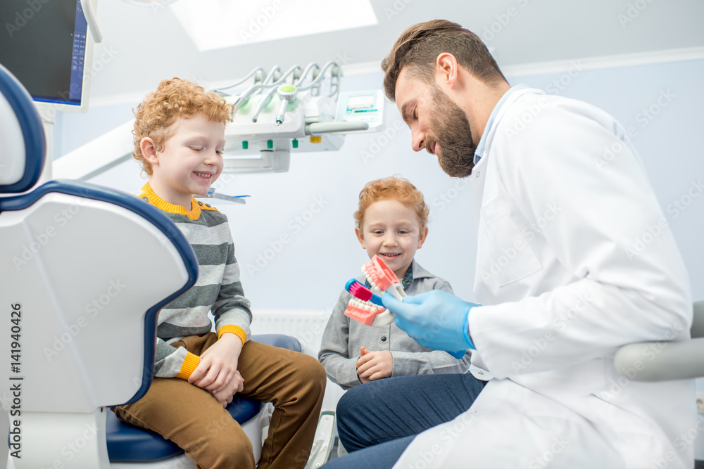 Obraz premium Children's dentist showing the boys how to brush teeth on artificial jaw at the dental office