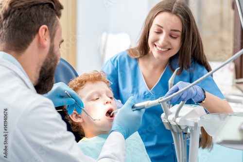Young boy during the dental procedure with dentist and assistant at the dental office photo