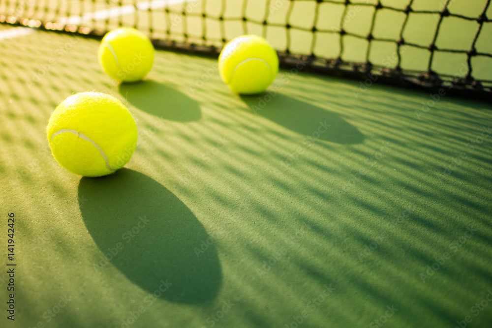 three tennis balls on green and red hard court with shadow from net