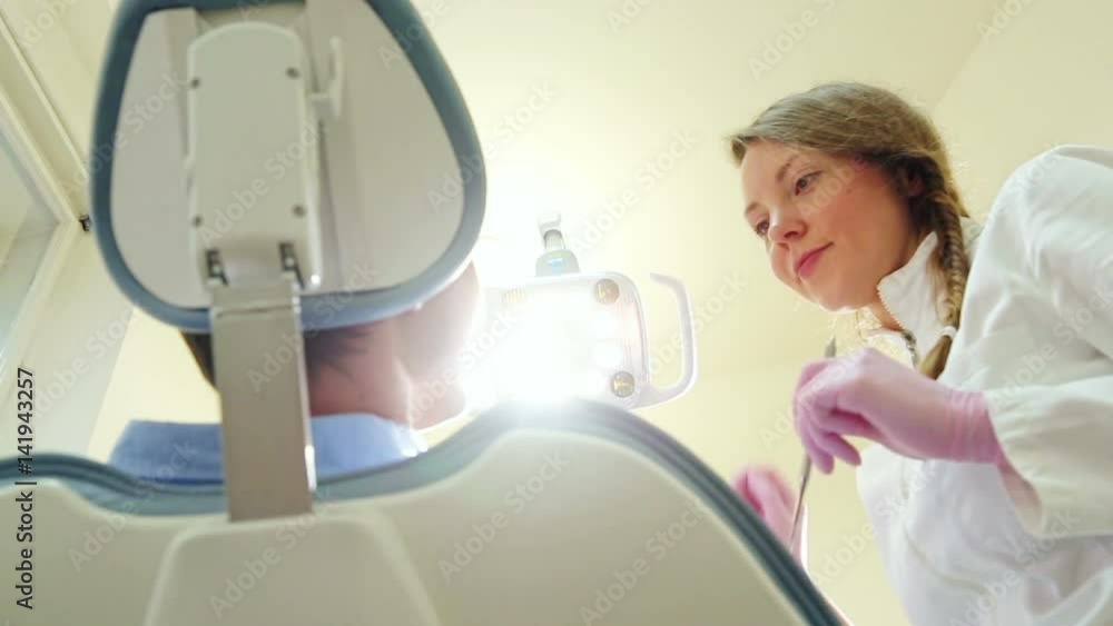 Friendly female dentist turning on lamp and examining teeth of her male patient Friendly female dentist turning on lamp and examining teeth of her male patient