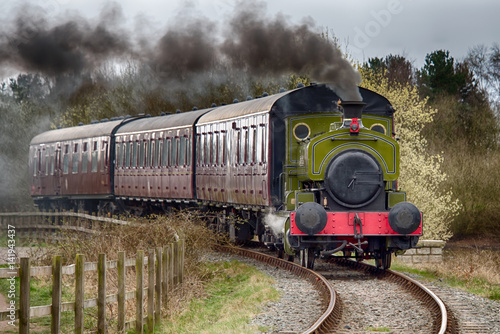 A steam train locomotive traveling forward with smoke emerging from the funnel.