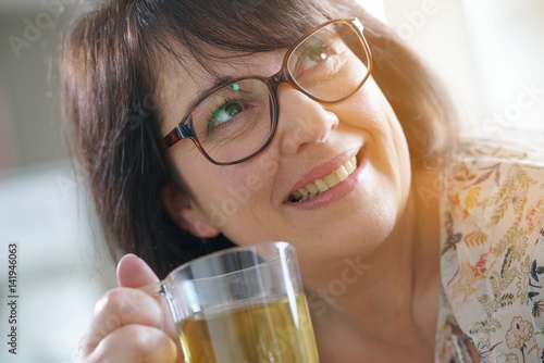 Fotografia Smiling mature woman with eyeglasses drinking infusion