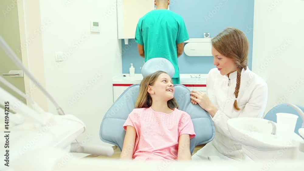 Friendly female dentist talks with young patient, male surgeon does routine check up