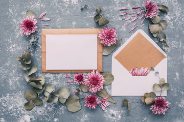 Flat lay workspace. Wedding invitation cards, craft envelopes, pink and red roses and green leaves on white background. Overhead view, top view