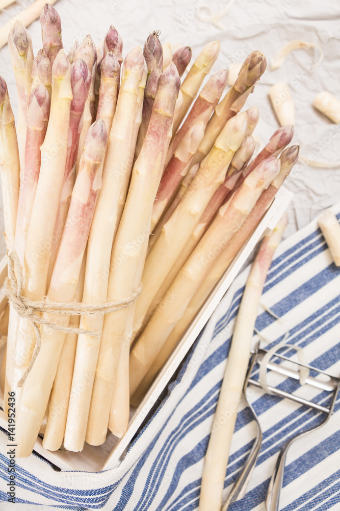 Bunch of white asparagus in box, on crumpled paper with metallic peeler and kitchen towel. Bunch of white asparagus in box, on crumpled paper with metallic peeler and kitchen towel.