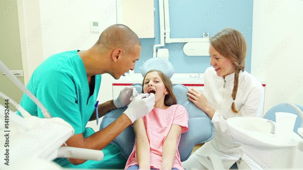 Friendly woman dentist talks with young patient while male surgeon examines her Friendly woman dentist talks with young patient while male surgeon examines her
