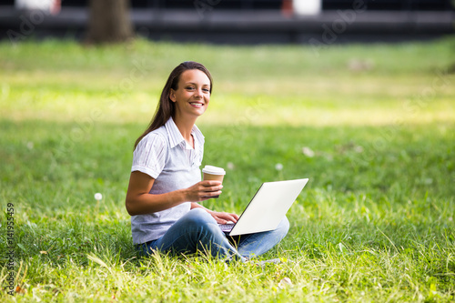 Beautiful businesswoman is drinking coffee and using laptop while resting from work at the park.