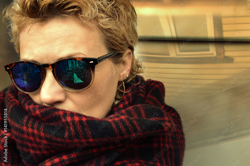 Portrait of a forty years old woman with short blond hair in sunglasses and a shawl
