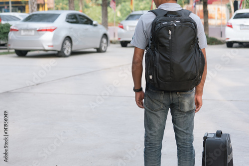 Asian man waiting for taxi on the car parking , tourist commuter with suitcase and backpack.