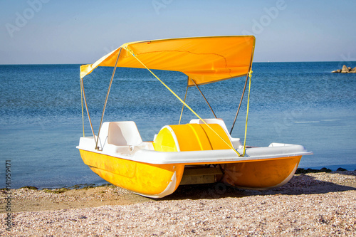 Yellow pedal catamaran boat with tent on a sea coast on a sunny day