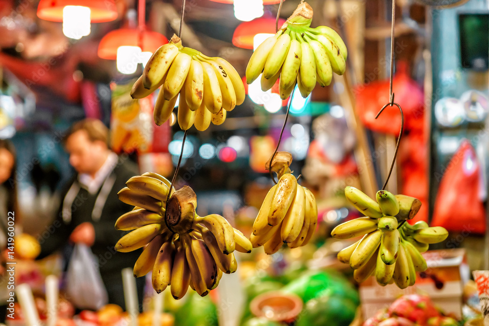 Asian street agricultural markets abound with different sorts of ripe fresh fruits. Bunches of yellow bananas hang at the shopboard