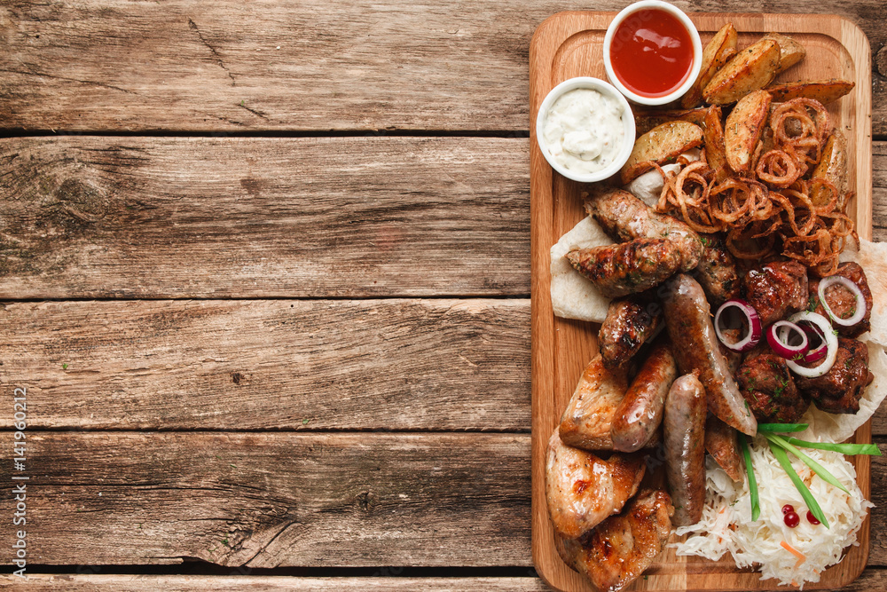 Mix of delicious tasty grilled meat free space. Snacks for beer served with pita bread, fried potato wedges,onion rings and sauerkraut on rustic wooden table. Restaurant menu photo. Mix of delicious tasty grilled meat free space. Snacks for beer served with pita bread, fried potato wedges,onion rings and sauerkraut on rustic wooden table. Restaurant menu photo.
