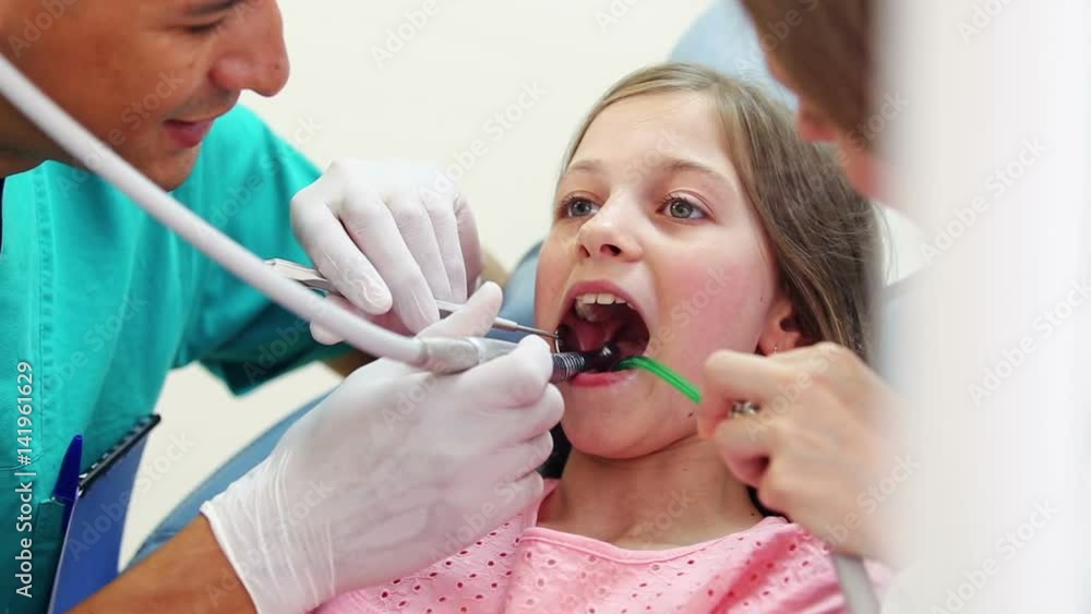 Female dentist and male surgeon fixing teeth of cute little girl, she's showing thumbs up, graded Female dentist and male surgeon fixing teeth of cute little girl, she's showing thumbs up, graded