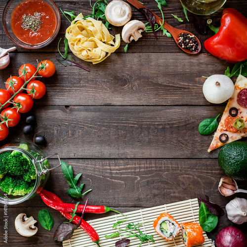 Frame with vegetables, pizza, sushi rolls, pasta and sauce on wooden background. Flat lay. Food frame