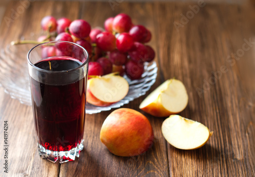 Grape juice in a glass beaker  grapes and apples on a wooden background. Fruit mix