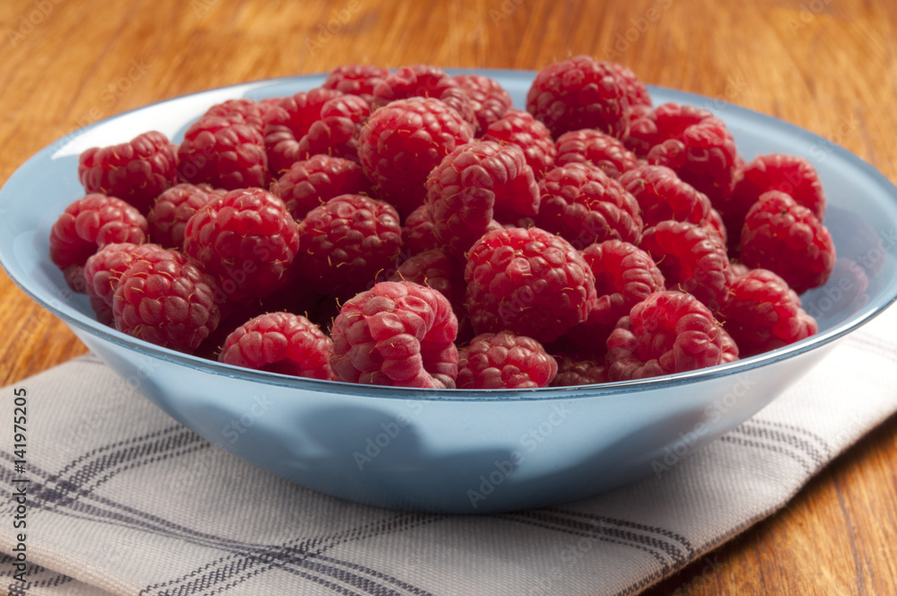 a blue bowl filled with red raspberries over vintage rustic dishtowel on wood table a blue bowl filled with red raspberries over vintage rustic dishtowel on wood table