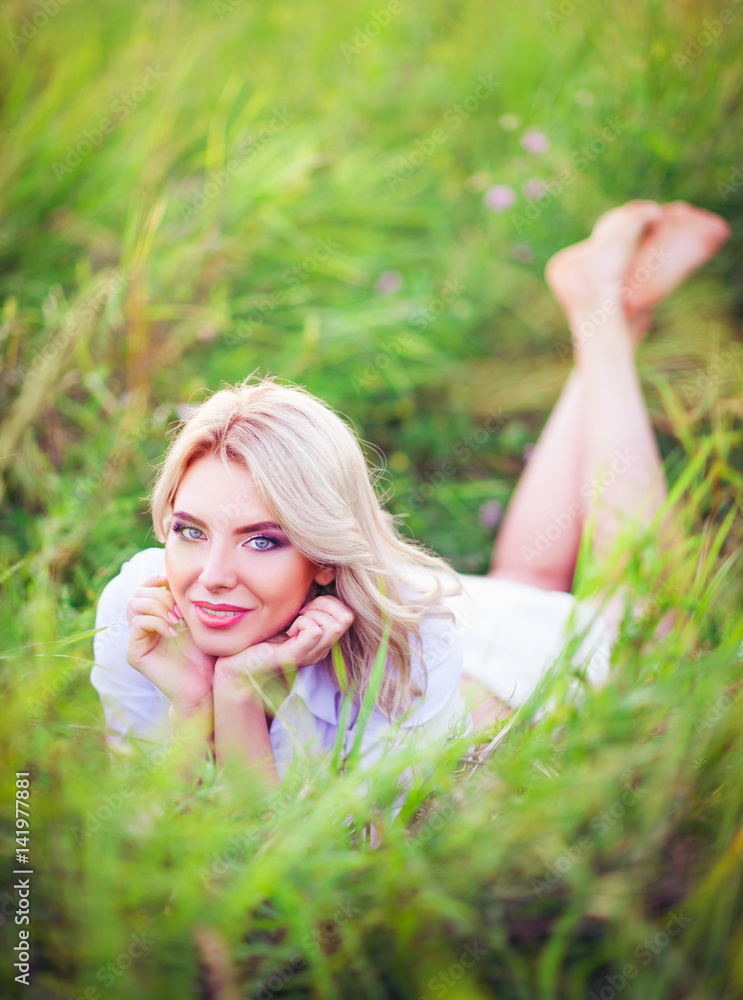 Smiling beautiful young woman lying among green grass Smiling beautiful young woman lying among green grass