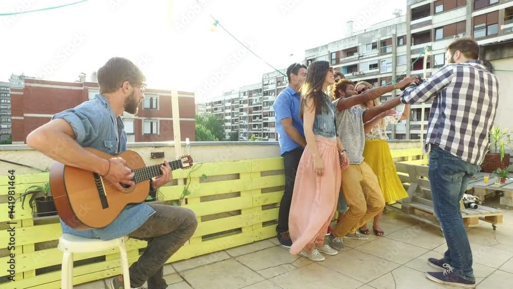 Group of smiling people taking photos while young musician playing guitar on the rooftop terrace Group of smiling people taking photos while young musician playing guitar on the rooftop terrace