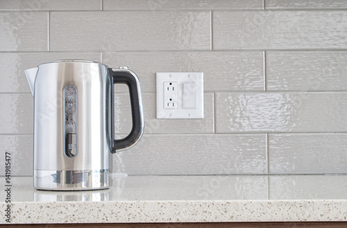 Modern electric stainless steel kettle on a granite counter top against a ceramic background photo