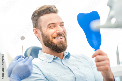 Handsome male patient looking at his beautiful smile sitting at the dental office photo