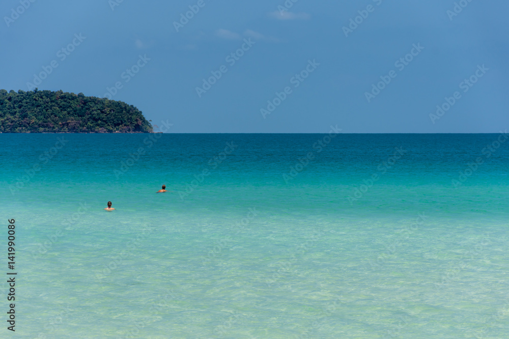 People in a tropical sea with headland on the horizon.