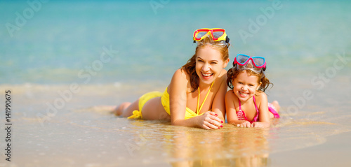 Foto Happy family mother and chid daughter in masks on beach in summer