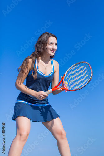 Girl with tennis racquet in hands posing against clear sky © azazello