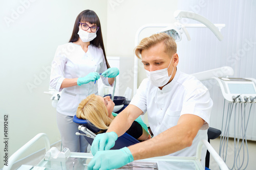 The dentist man and  assistant woman are treating  teeth to  client in dental office.